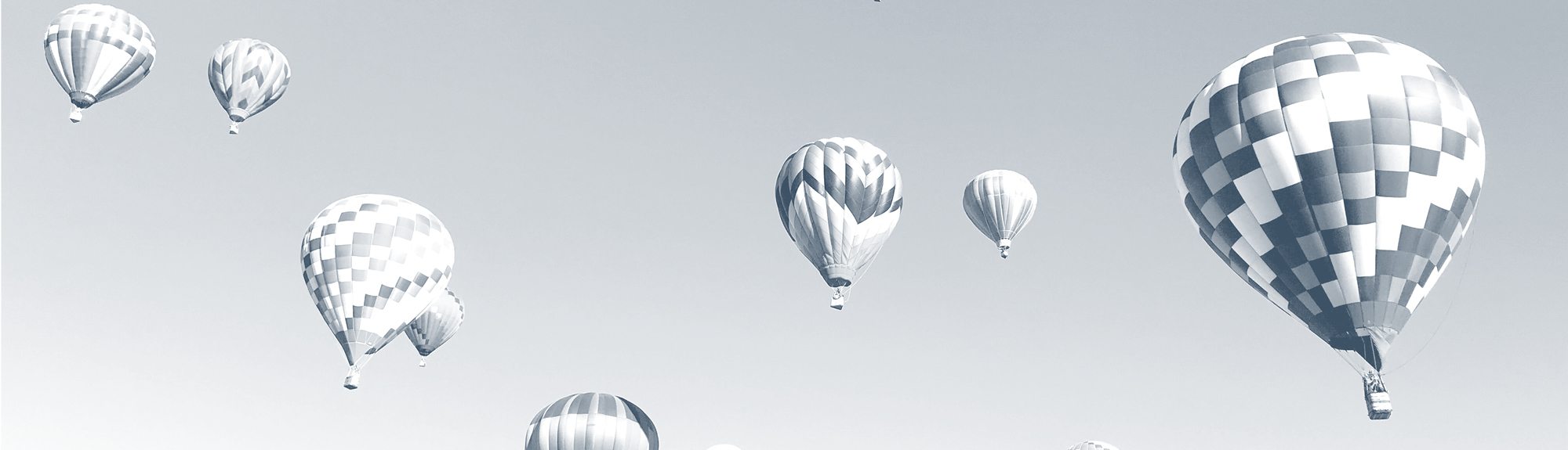 Grey image of several hot air balloons in the sky.