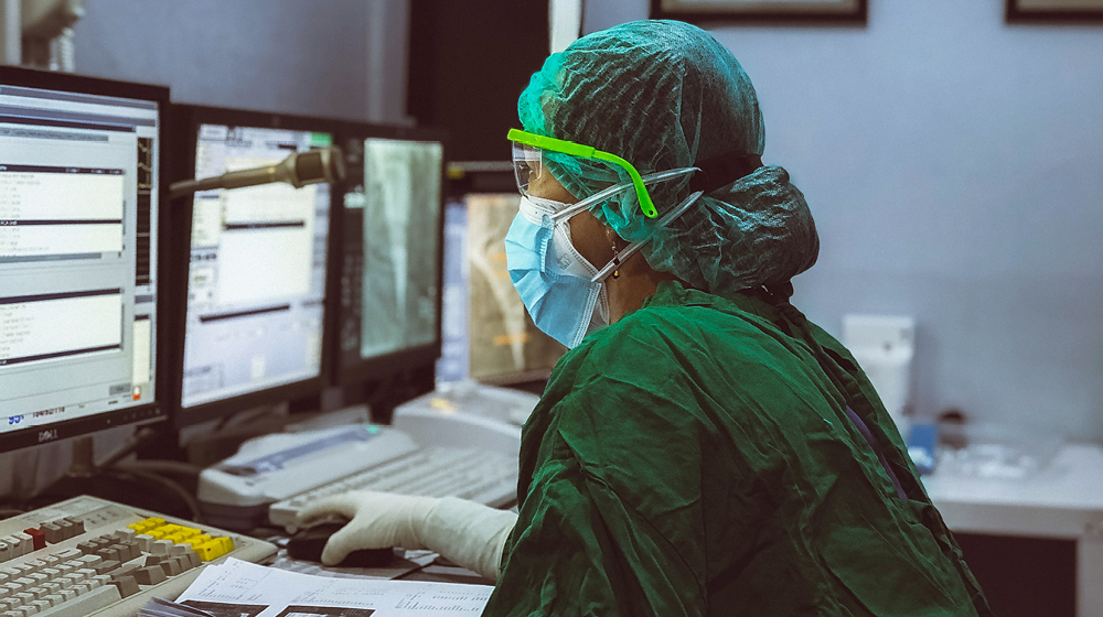Image of someone wearing medical protective gear working on a computer.