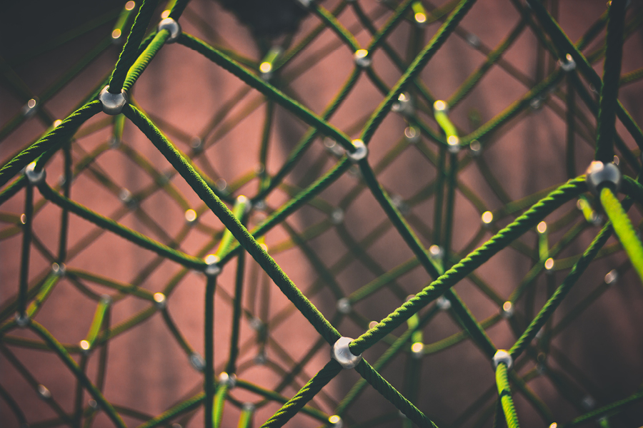Shallow depth-of-field abstract photo of an organic, interconnected 3 dimensional lattice consisting of segments of green rope and silver metallic nodes at each junction.